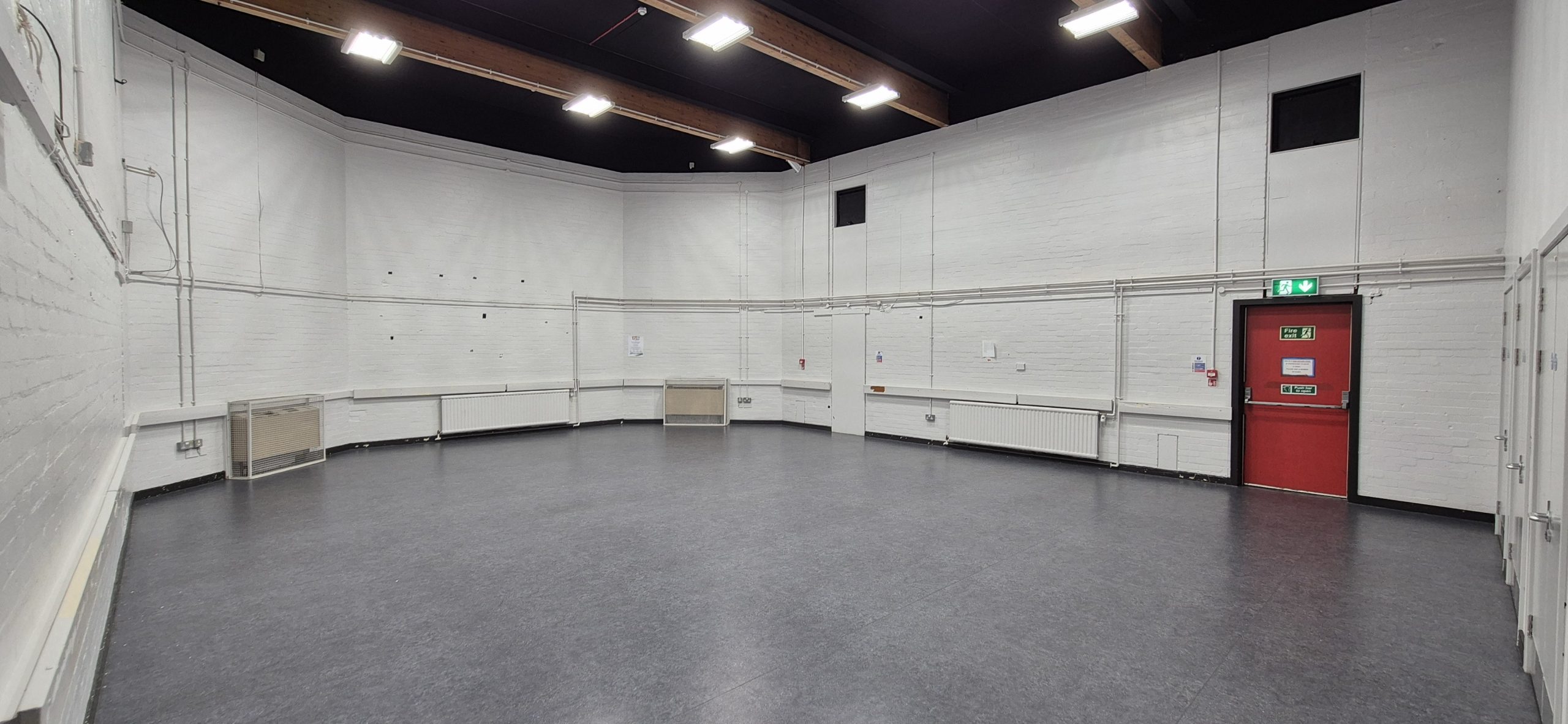 Assembly Hall at Whitburn Community Centre — a large, open hall with high ceilings, exposed timber roof beams, industrial strip lighting, and a clear grey floor