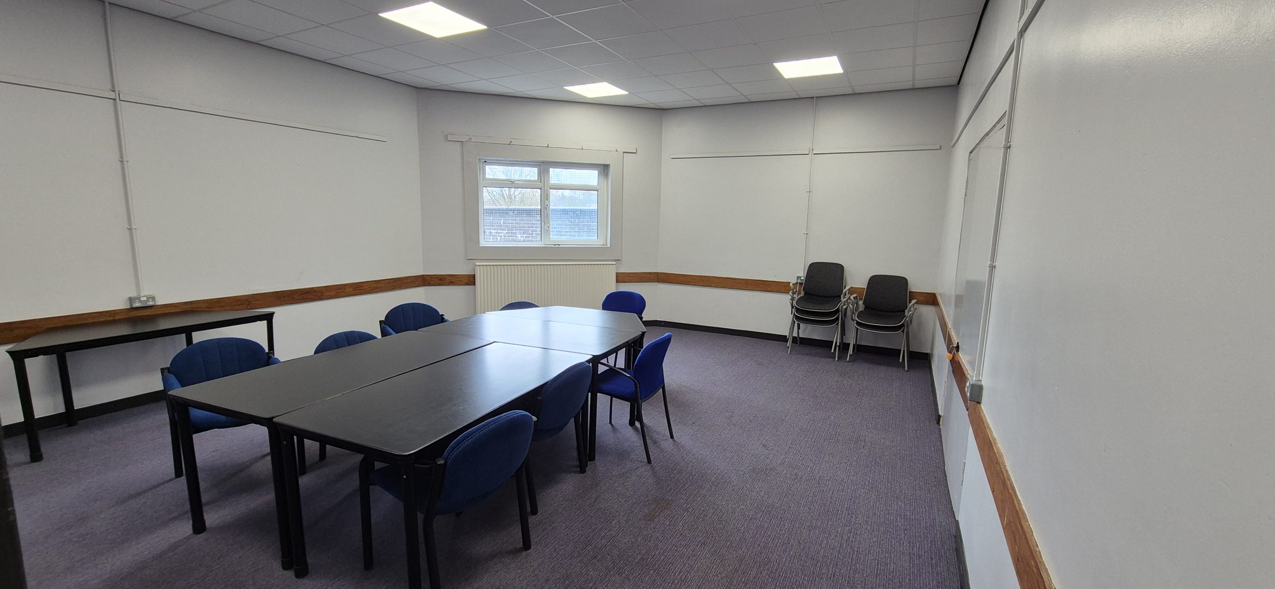 Quiet Room at Whitburn Community Centre — well-lit meeting room with a central boardroom table, blue chairs, whiteboard, and TV screen